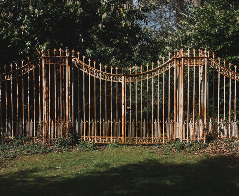 A decorative wrought iron gate framed by vibrant green trees in a serene outdoor setting.