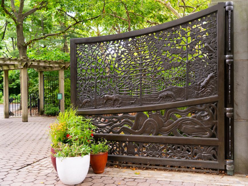 Ornate metal gate with nature motifs in a lush park with vibrant flowers.